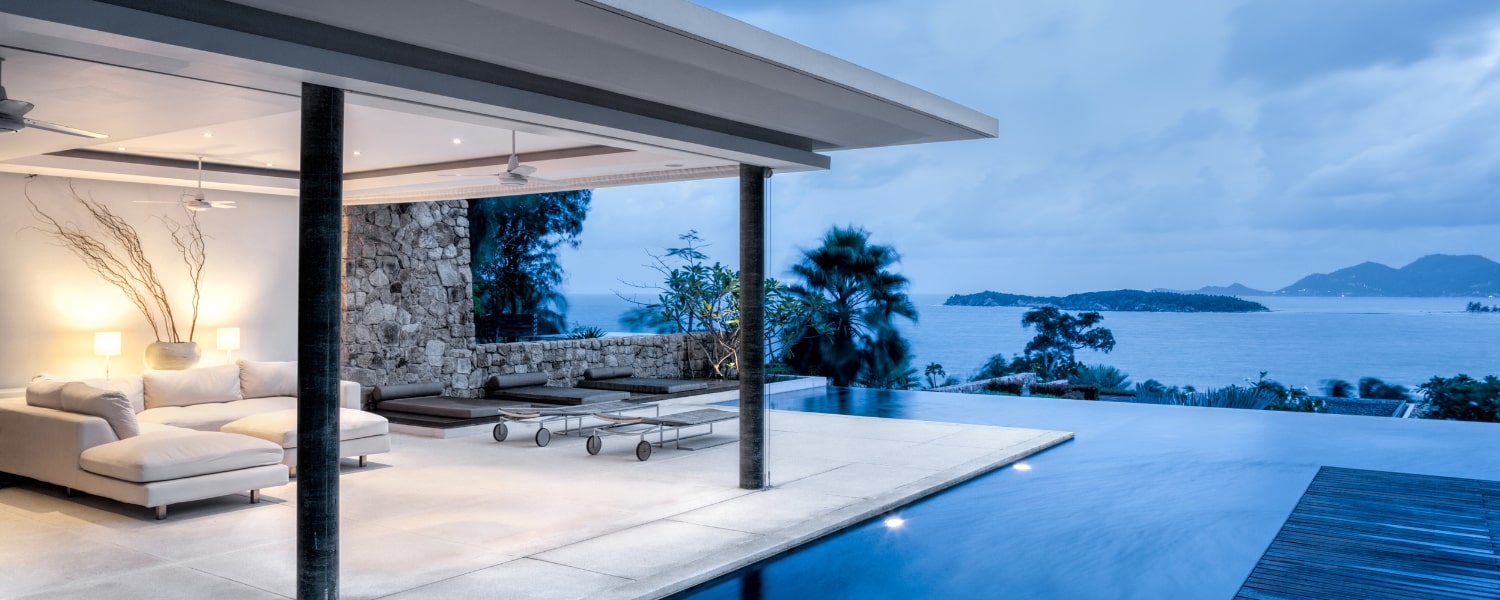Modern coastal villa with an infinity pool overlooking a tropical seascape at twilight, featuring sleek outdoor furniture and a tranquil ambience.